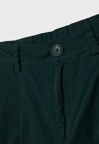 Ceinture de pantalon vert foncé avec fermeture par bouton, passants de ceinture et coutures visibles sur fond uni.