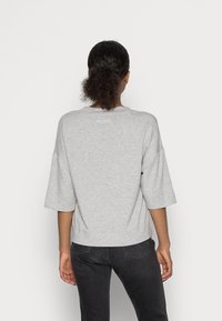 Szary, krótki sweatshirt z luźnym krojem. Materiał jest miękki, z okrągłym dekoltem i małym logo nadrukowanym na plecach.