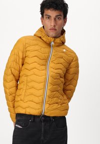 Giacca gialla imbottita con design trapuntato a zigzag, chiusura frontale con cerniera e striscia multicolore, e cappuccio attaccato.
