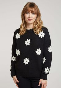 Pull en maille noire avec des motifs de fleurs blanches, doté d'un col rond et de manches longues. Texture douce avec des poignets et un ourlet côtelés.