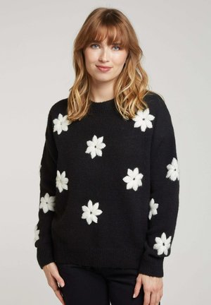 Pull en maille noire avec des motifs de fleurs blanches, doté d'un col rond et de manches longues. Texture douce avec des poignets et un ourlet côtelés.