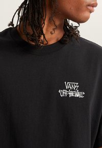 Camiseta negra de manga larga con cuello redondo y logo blanco "VANS OFF THE WALL" en el lado izquierdo del pecho, fabricada en suave material de algodón.