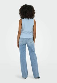 Ljusblå ärmlös topp med en texturerad yta, kombinerad med högmidjade, vida ljusa jeans. Svarta klackskor synliga.