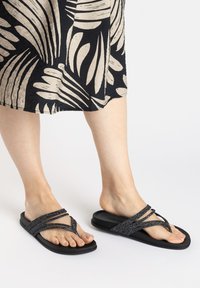 Schwarze Flip-Flops mit glitzernden Riemen, flacher Sohle, einfachem Zehenstegdesign und bequemem Sitz.