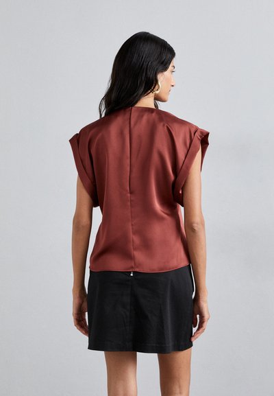 Blusa de satén color óxido con mangas cortas, un escote redondeado y una costura central en la parte posterior, combinada con una falda negra. Textura suave.