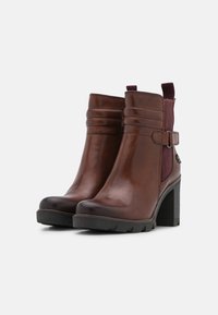 Bottines en cuir marron avec un bout arrondi, des panneaux élastiques sur les côtés, une sangle décorative et un talon épais. Fini texturé avec une surface lisse.