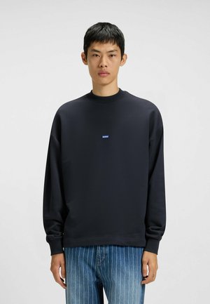 Dark navy sweatshirt with a round neck, long sleeves, and a small blue "HUGO" logo on the chest, paired with light blue pinstriped jeans.