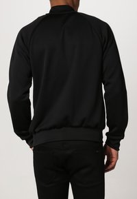 Black sweatshirt with a ribbed collar and hem, featuring long sleeves and a smooth texture; has white detailing on the sides.