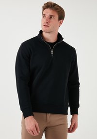Black pullover sweatshirt with a zippered mock neck, crafted from soft fabric. Features long sleeves and a fitted waist.