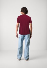 T-shirt bordeaux à manches courtes vu de dos, associé à un jean large bleu clair. Le t-shirt a un design simple et une texture lisse.