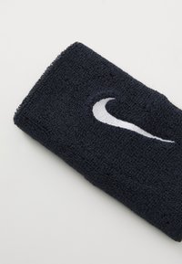 Fascia in spugna nera con il logo Swoosh bianco della Nike ricamato su uno sfondo bianco semplice.