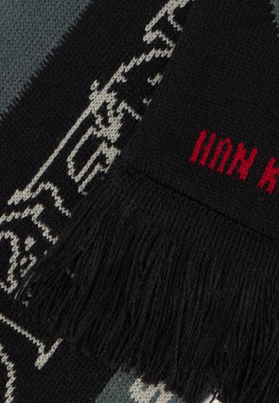 Melnas un pelēks adīts šalle ar bārkstīm malās, izteiksmīgu sarkanu tekstu un rakstainu abstraktu formu dizainu kontrastējošās krāsās.