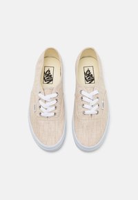 Zapatillas de lona beige claro con cordones blancos, que cuentan con ojales circulares y una suela de goma. Logo impreso en la plantilla.