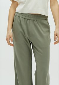 Pantalones ligeros de color verde oliva con una cintura elástica, bolsillos laterales y un corte holgado, fabricados con una tela suave.