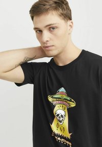 Sort bomulds t-shirt med et farverigt grafisk print af et UFO og et kranium, med markante accenter i gul, grøn og pink. Korte ærmer, rund hals.