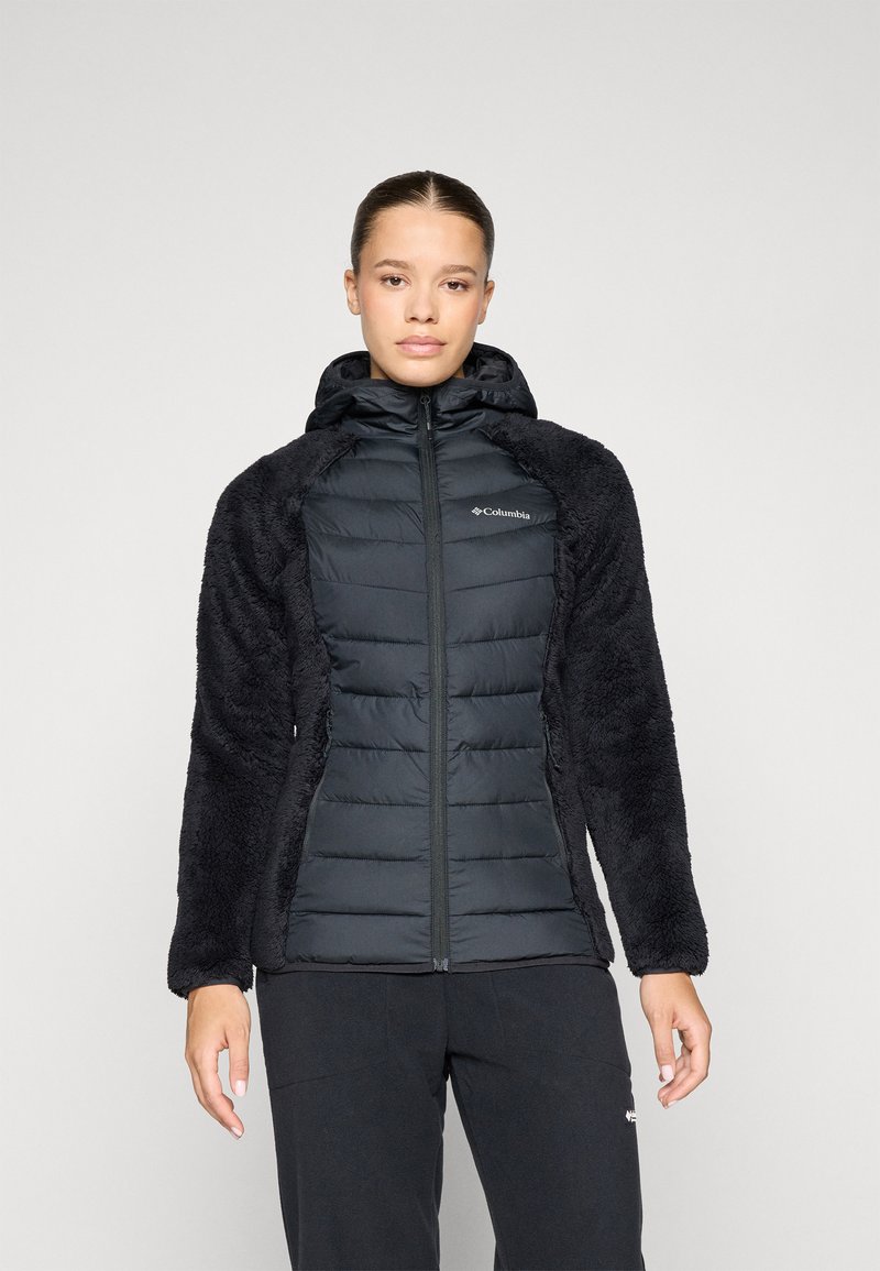 Svart zip-up jakke med polstrede og faux pels deler; har hette, kontrasterende teksturer, og en glatt overflate på torsoen.
