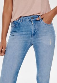 Ljusblå denim skinny jeans med en mid-rise passform, femficksdesign och subtila slitna detaljer vid knäna. Tyget har en jämn textur.