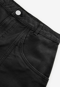 Pantalon en denim noir avec un bouton argenté, doté de poches latérales et de coutures apparentes sur le tissu. Texture lisse et coupe standard.