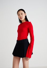 Haut rouge à manches longues en tissu extensible, associé à une mini-jupe en denim noir avec un ourlet effiloché et un design plissé.