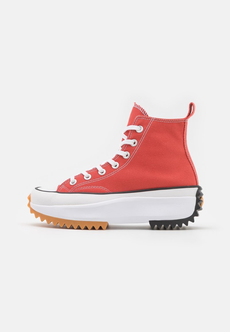 Roter High-Top-Sneaker aus Segeltuch mit weißen Schnürsenkeln, ausgestattet mit einer dicken weißen und schwarzen Plateausohle mit gezacktem orangem Rand.