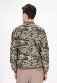 Camouflage bomberjack gemaakt van lichtgewicht stof; heeft een groen, zwart en beige pixelachtig patroon; ribgebreide manchetten en zoom.