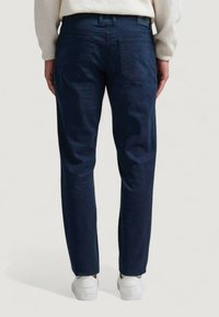 Pantalones azul marino de algodón con una textura suave, que cuentan con dos bolsillos traseros y una cintura con trabillas para el cinturón. Llevados con zapatillas blancas.