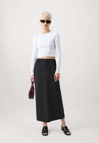 Fehér bordázott, hosszú ujjú crop top, fekete maxi szoknya, fekete nyitott orrú mules cipők és egy bordó kézitáska. Kiegészítők közé tartozik fekete napszemüveg és karika fülbevalók.