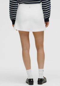 Weiße Skort mit ausgestelltem Design, hergestellt aus glattem Material. Verfügt über einen Bund und ein Logo-Detail auf der Rückseite, geeignet für aktive Kleidung.