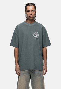 Zielona bawełniana koszulka z okrągłym dekoltem, krótkimi rękawami i fakturowanym materiałem. Posiada białe logo graficzne na lewej piersi.