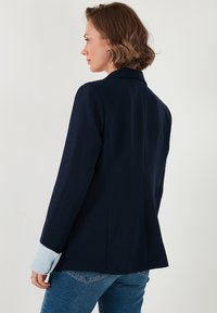 Tumed blazer, mille struktuurse disainiga, helesiniste soonikkohtadega, kohandatud siluetiga ja sileda kangatekstuuri korral.