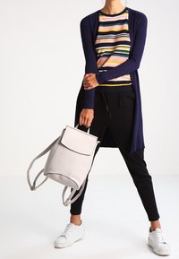 Laivastonsininen ribbineuleinen neuletakki, monivärinen raitainen paita, mustat housut, valkoiset tennarit ja vaaleanharmaa nahkainen reppu läppäkannella.