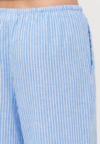 Calças listradas em azul claro com um corte relaxado, feitas de um tecido suave. Apresenta listras brancas verticais e uma cintura elástica com bolsos laterais.