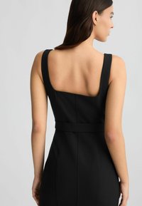 Abito nero con spalline larghe, schiena quadrata, silhouette aderente e vita cintrata con dettagli di cucitura in evidenza. Tessuto liscio.