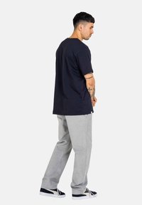 Navy cotton t-shirt with short sleeves, paired with light grey pants. The model stands sideways, showcasing a simple and relaxed fit.