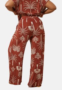 Röda byxor i mjukt stoff med vit palmträdstryck. Bred ben design, elastisk midja och strukturerad yta.