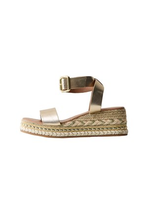 Gouden metalen sleehak sandaal met enkelbandje en gesp, voorzien van een gevlochten jute plateauzool en decoratieve kraalaccenten.