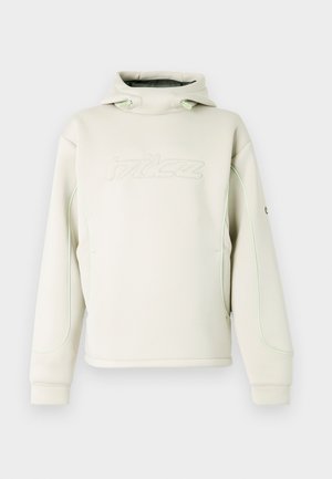 Kreemjas kapuutsiga pusa, millel on kõrge krae ja tõmbelindid, rinnal peen reljeefne logo ning rohelised triibud varruka ja külgede ääres.