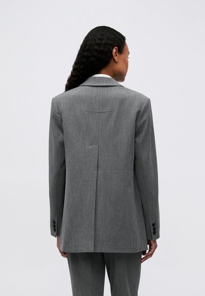 Blazer gris ajusté avec une silhouette structurée, revers crantés et fente simple à l'arrière. Présente des poignets à boutons et une texture lisse.