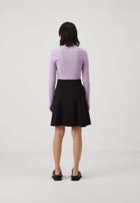 Lilac fitted long-sleeve top paired with a black skater skirt. Skirt has a smooth texture and falls to mid-thigh. Black sandals with decorative accents.