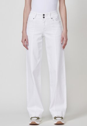 Jeans de pierna ancha blancos con cintura alta, cierre de dos botones, bolsillos laterales y detalles de costura sutiles, combinados con zapatillas blancas y verdes.