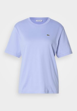 Lys lilla bomull t-skjorte med rund hals og korte ermer. Har en liten brodert Lacoste-logo på brystet.