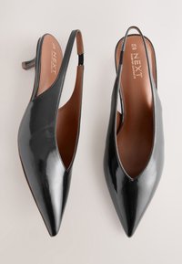 Mustad lakknahast tagant rihmaga kontsakingad, terava ninaga, madala kontsaga ja lõigatud disainiga. Sile tekstuur, pruun sisetald, millel on silt "NEXT".