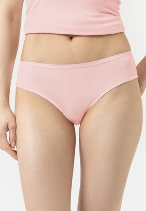 Woman wearing light pink cotton underwear and matching cropped top, shown from midriff to upper thighs against a white background.