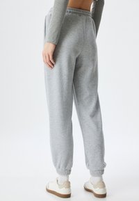 Grijze, zachte fleece joggers met een elastische tailleband en aangesloten enkels, gecombineerd met witte en tan sneakers en een geribde grijze longsleeve top.