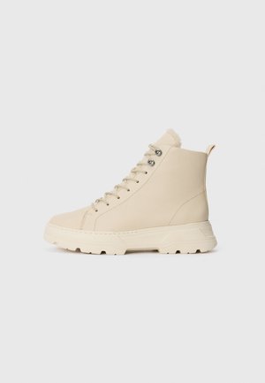 Beige højt sneakers med tyk sål, metaløjer, snørebånd og trækflap bagpå, vist i profil på en ensfarvet baggrund.