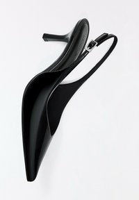 Escarpin slingback à talon haut brillant noir avec un bout pointu, une fine bride et une petite boucle argentée sur fond blanc uni.
