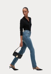 Maglione ripbutton nero, jeans azzurri a vita alta, tacchi slingback neri e una borsa nera con un accento dorato.