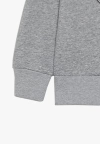 Tejido de sudadera gris claro con puños acanalados, que presenta una textura suave y un ajuste relajado. Los detalles de las costuras realzan la simplicidad del diseño.