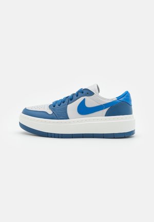 Zapatilla baja de piel blanca y azul, cordones azules y suela blanca gruesa con suela azul, vista lateral sobre fondo neutro.