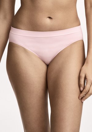Frau trägt nahtlose Hipster-Unterwäsche in Hellrosa, steht mit sichtbarem Oberkörper und oberen Oberschenkeln vor weißem Hintergrund.